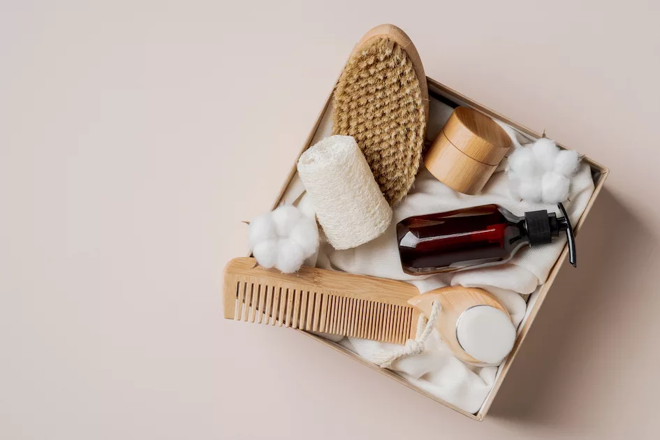 Beauty gift box with natural cosmetics set on beige background. Flat lay, top view present box with body brush, hair comb, shampoo, loofah, moisturizer cream.